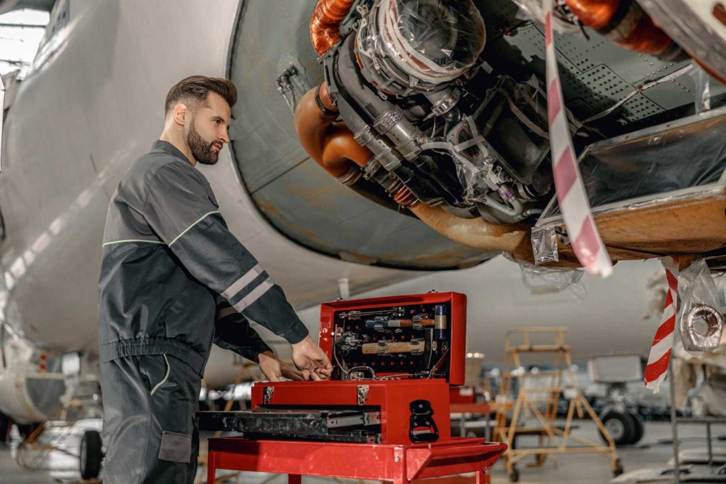 Male worker maintenance technician putting instrument in tool box while standing near airplane at repair station